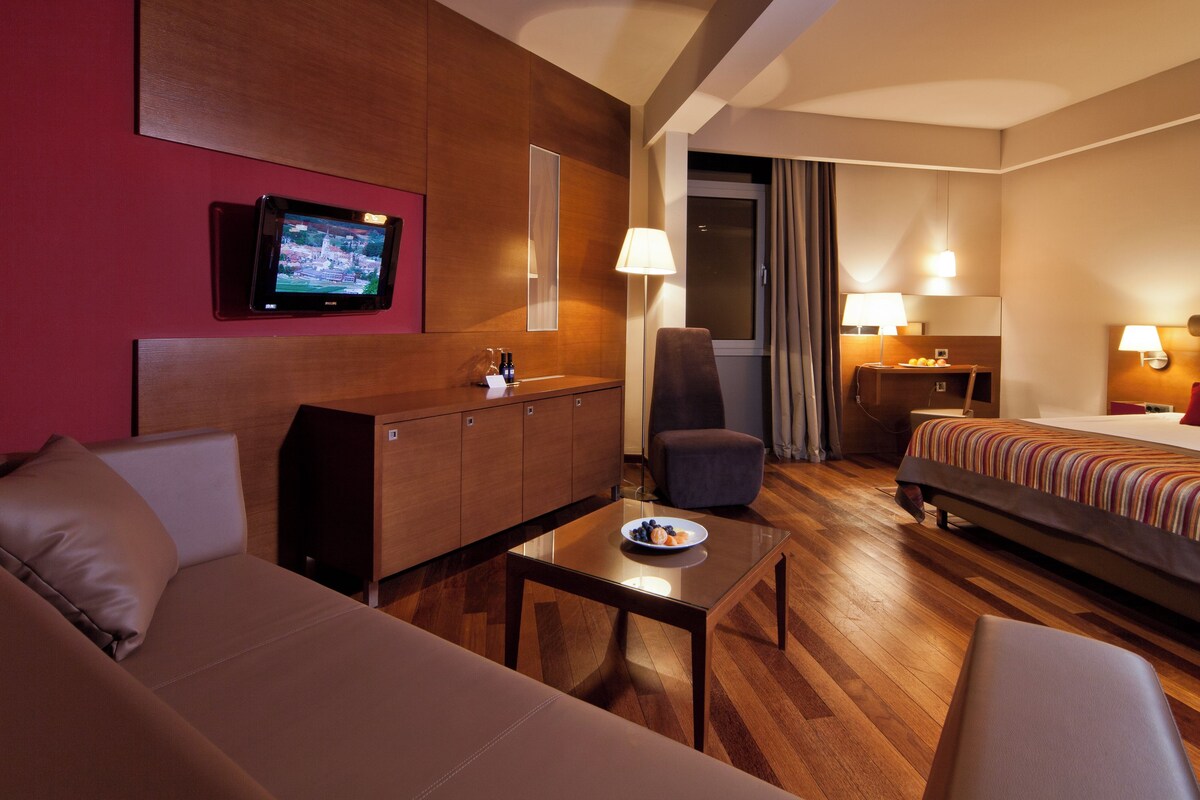 A hotel room with a bed, a sofa, a desk, a TV, and a chair.