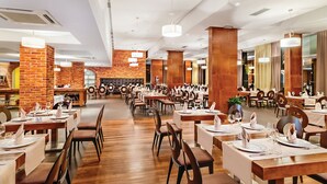 A spacious restaurant with high ceilings, exposed brick walls, and modern pendant lighting. Tables are neatly arranged with white tablecloths and set for dining. - Hotel Kaj (Marija Bistrica)