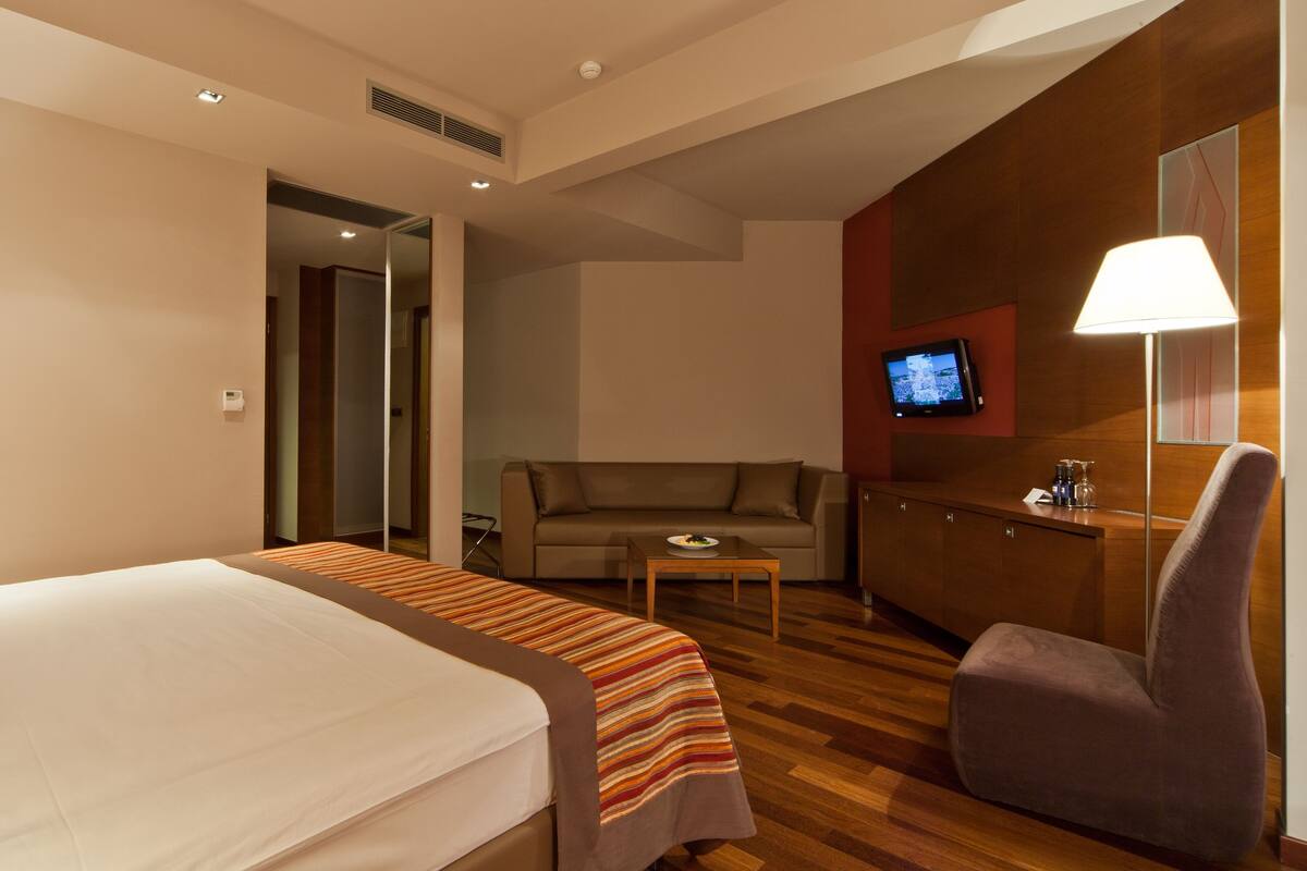 A hotel room with a bed, a sofa, a desk, and a TV.