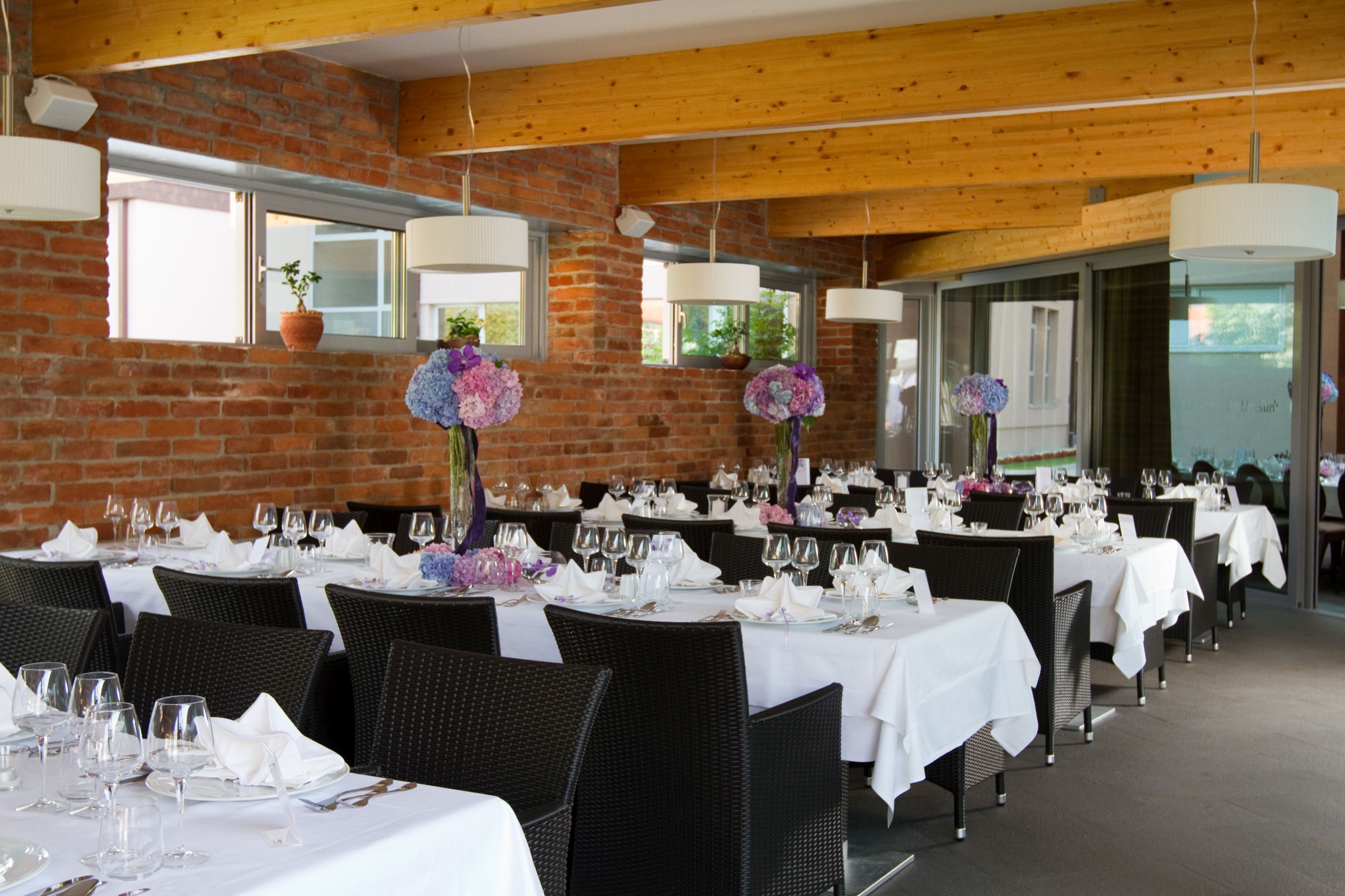 A restaurant with brick walls, wooden beams, and tables set with white tablecloths and silverware.
