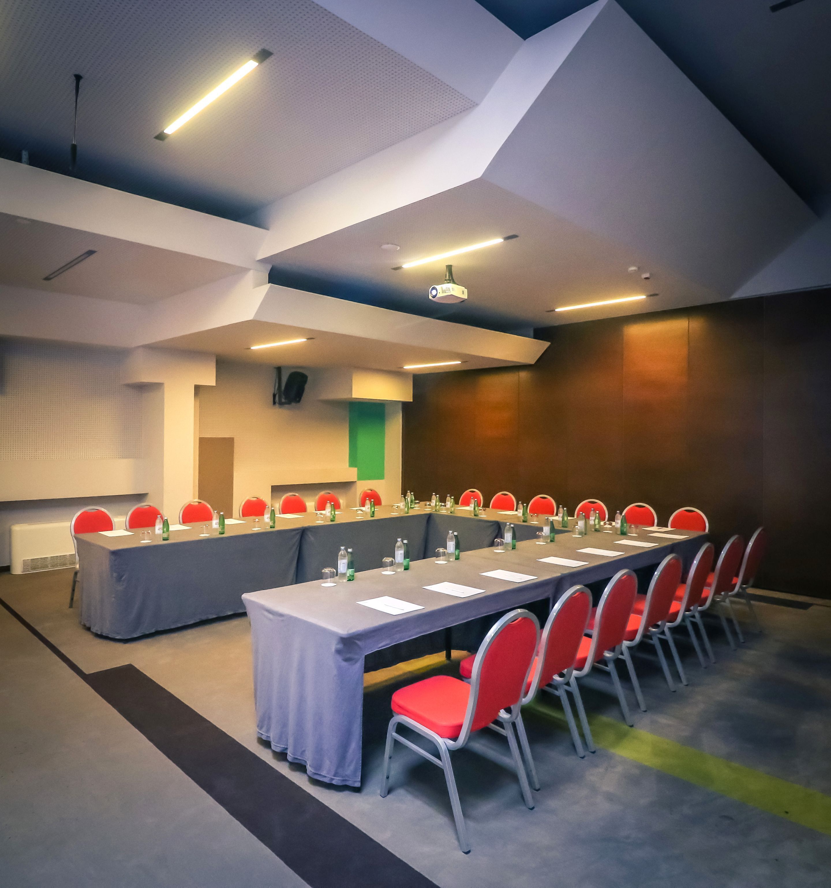 Une salle de conférence avec une longue table, des chaises rouges et un écran de projection.