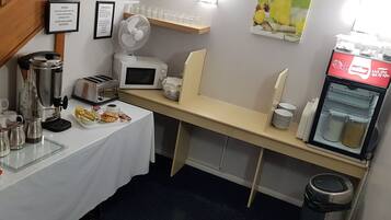 A kitchenette with a coffee maker, toaster, microwave, and a refrigerator with a beverage dispenser.