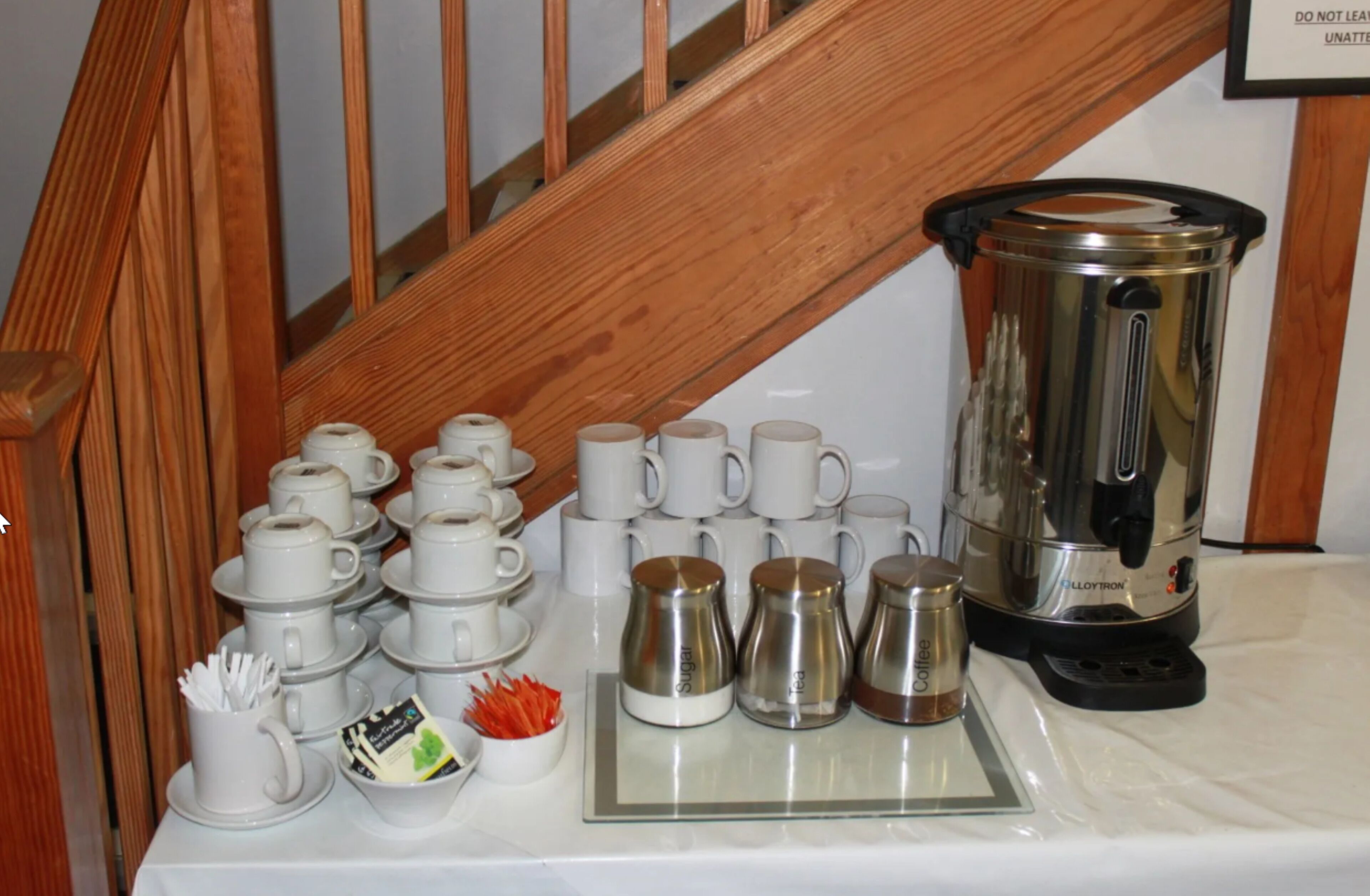Una estación de café con varias tazas, una jarra de café y sobrecitos de azúcar sobre una mesa.