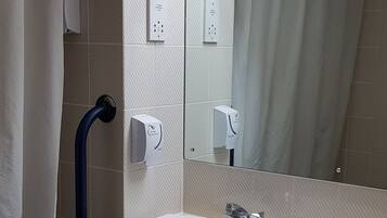 A bathroom with a white sink, a mirror, a shower curtain, a hand dryer, and a trash bin.