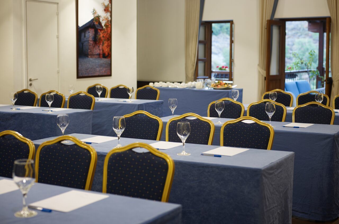 Un salón de conferencias con mesas dispuestas para reuniones, cada una con una silla y un vaso de agua.