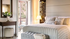 Un dormitorio ordenado con una cama grande, una mesita de noche con un jarrón de flores, una lámpara y vistas al exterior a través de un ventanal corredero.