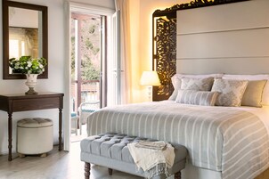 Un dormitorio ordenado con una cama grande, una mesita de noche con un jarrón de flores, una lámpara y vistas al exterior a través de un ventanal corredero.