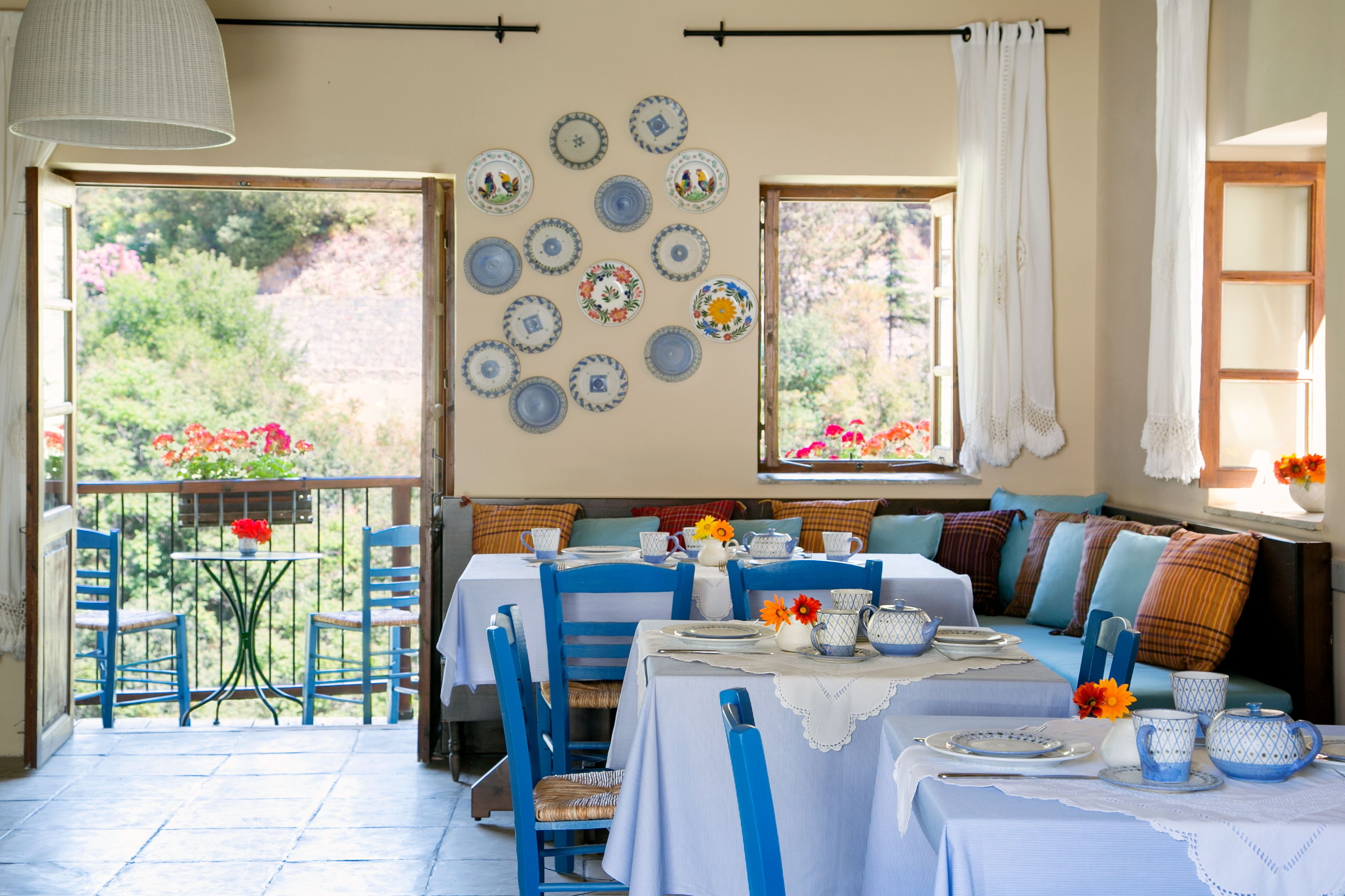 A dining area with a balcony, blue chairs, a table set with plates, cups, and a vase of flowers.
