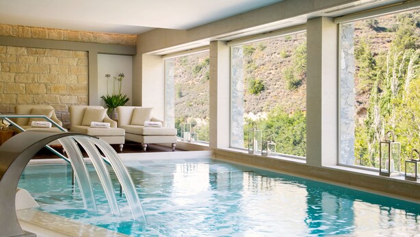 Zona de piscina con muro de piedra, un conjunto de sofás y vista a una ladera.