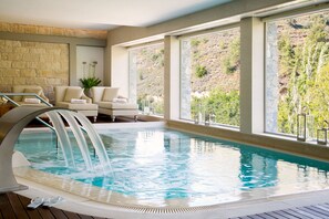 Zona de piscina con muro de piedra, un conjunto de sofás y vista a una ladera.