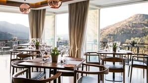 Un restaurante con mesas preparadas para comer, amplias ventanas que ofrecen vista a la montaña y un balcón con barandilla.