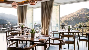 Un restaurante con mesas preparadas para comer, amplias ventanas que ofrecen vista a la montaña y un balcón con barandilla.