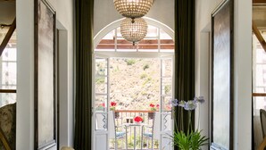 Un pasillo con una araña, bancos y vistas a un patio con sillas y flores.