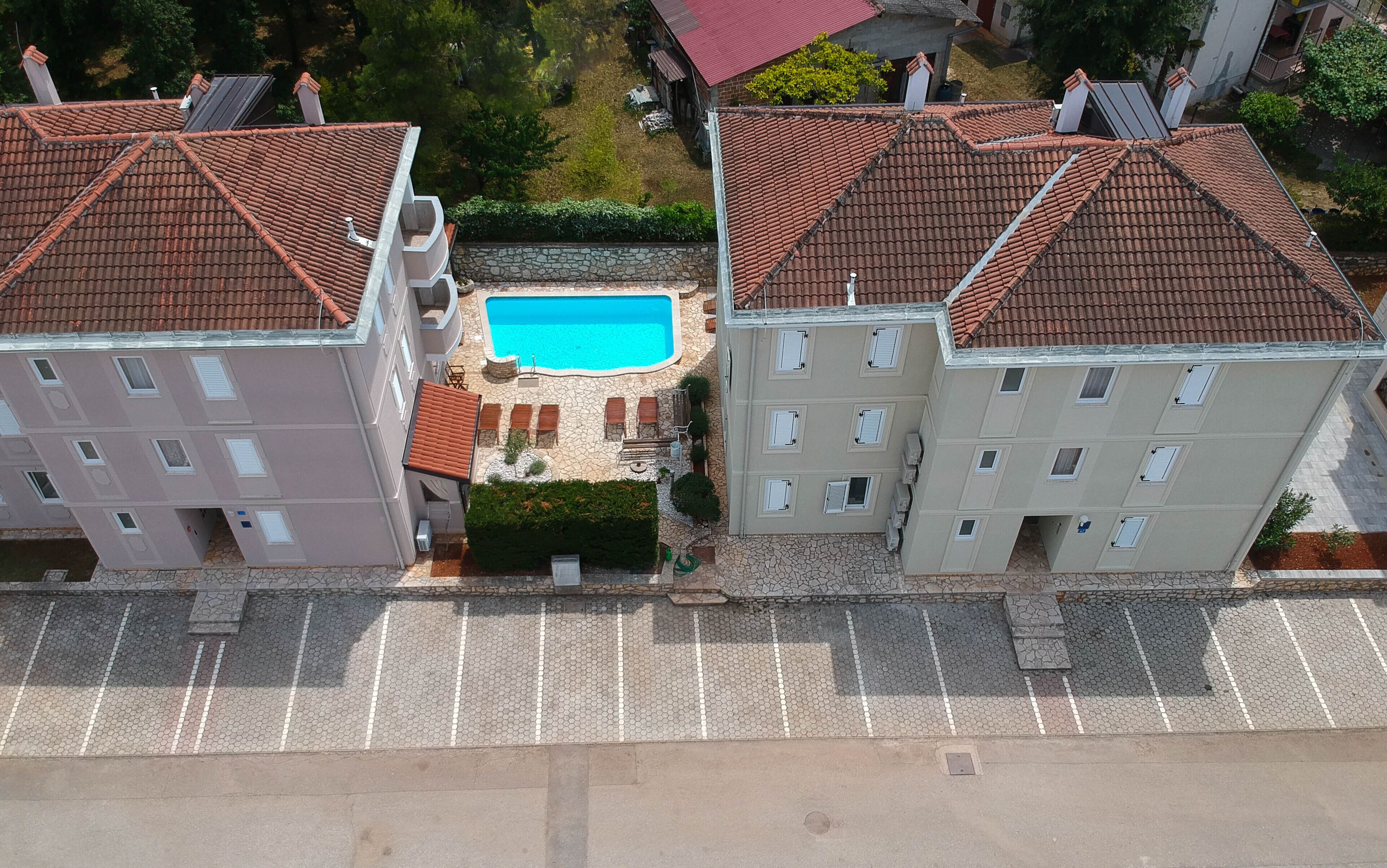 A residential building with a swimming pool surrounded by stone tiles and greenery.
