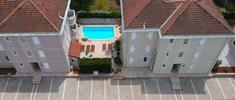 A residential building with a swimming pool surrounded by stone tiles and greenery.