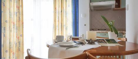 A dining area with a table set for two, a potted plant, and a window with curtains.