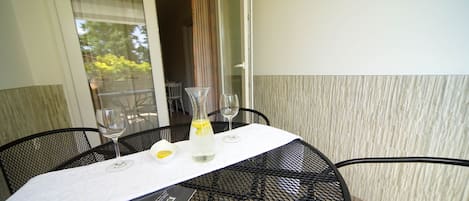 A table with a white tablecloth, two wine glasses, a bottle of water, and a menu on a metal table.