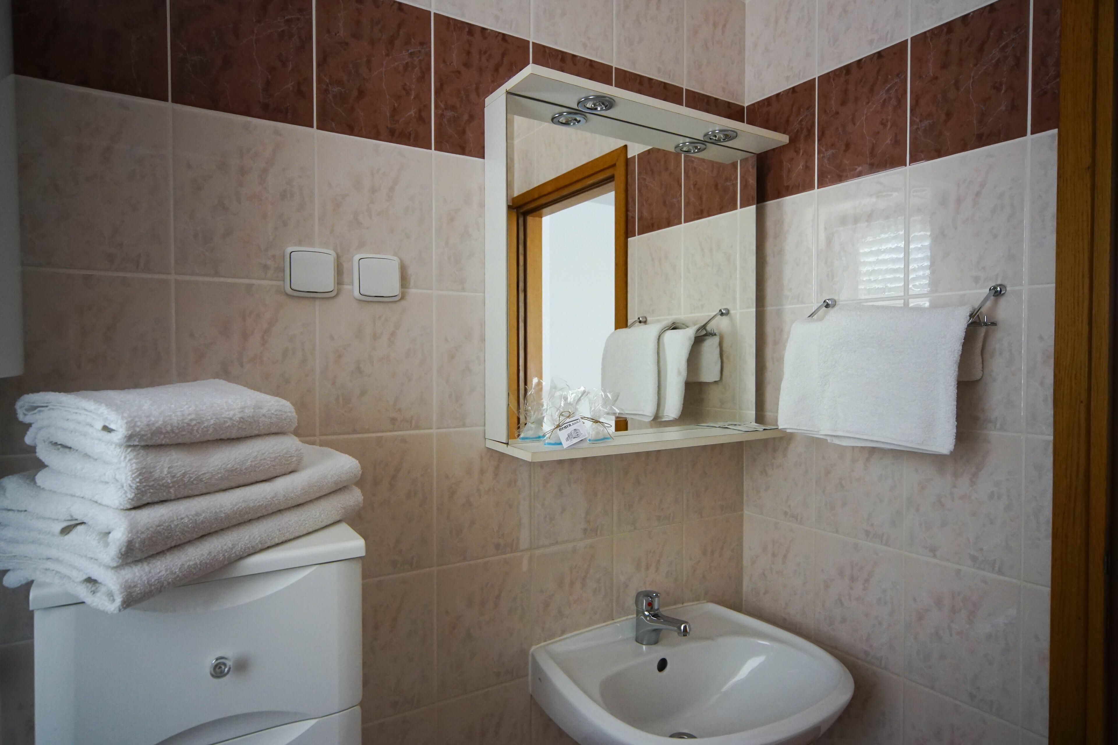 A bathroom with a white sink, a mirror, and a stack of white towels on a cabinet.