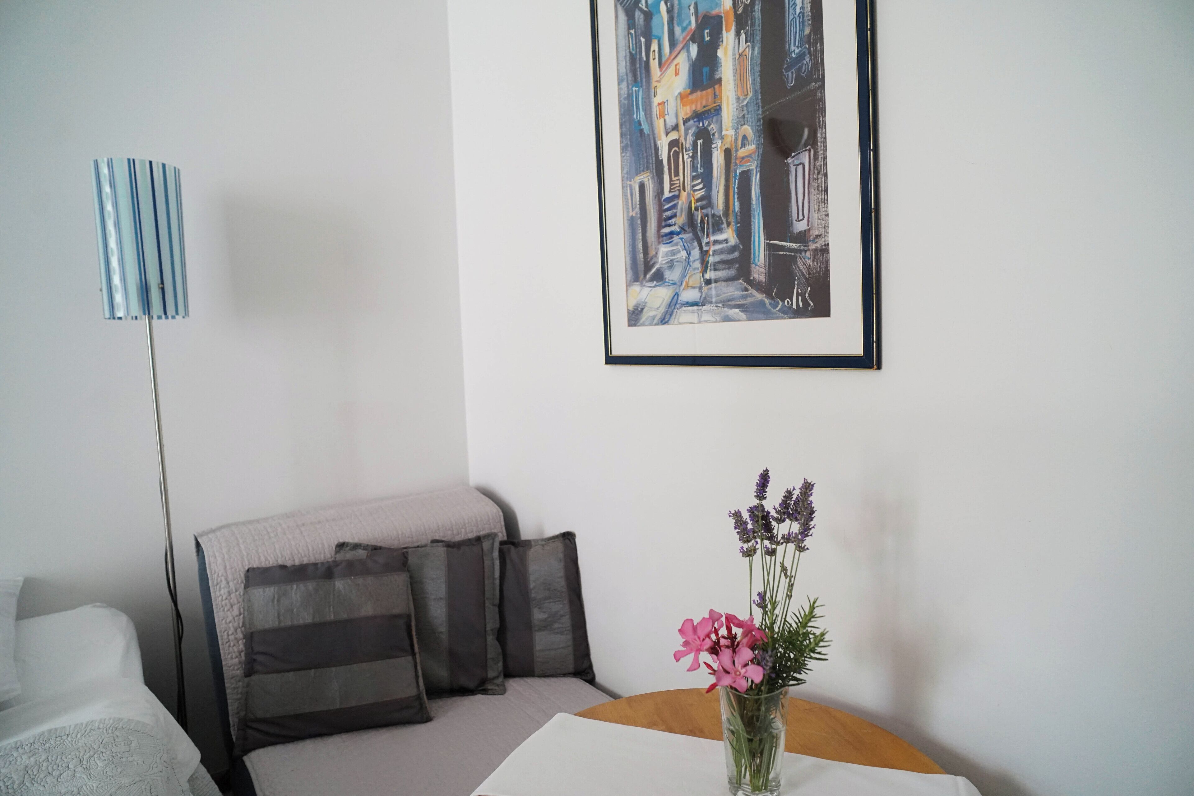 Una habitació amb un sofà, una taula amb un ram de flors, una làmpada i un quadre amb marc a la paret.