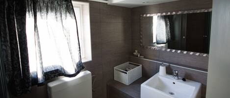 Een moderne badkamer met een wit wastafelmeubel, een spiegel en een raam met decoratieve gordijnen.