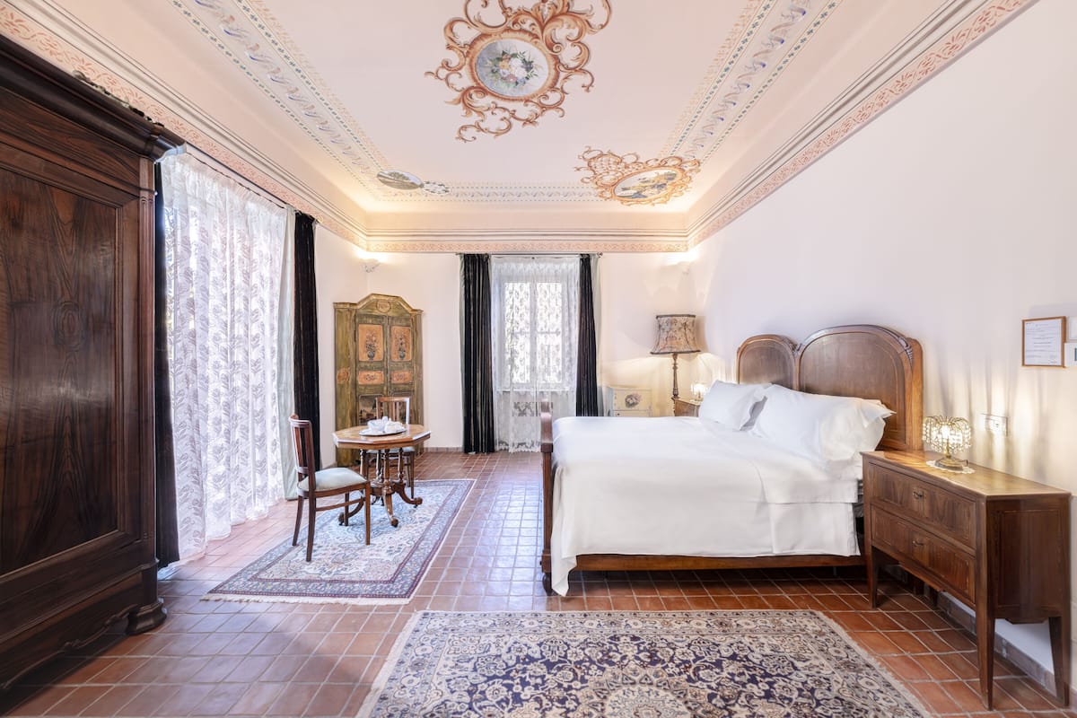 A bedroom with a large bed, wooden furniture, and a decorative ceiling.