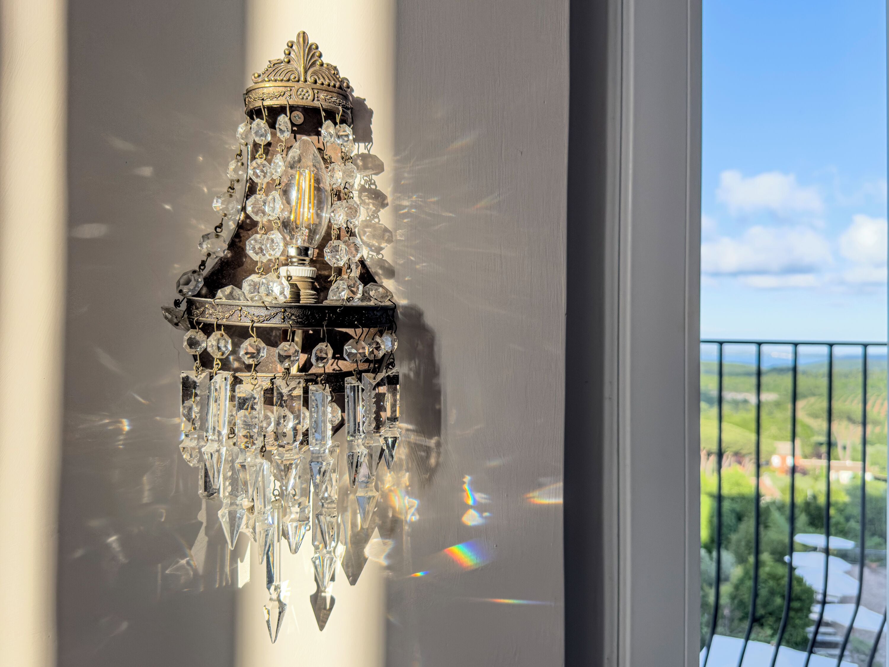 A chandelier with multiple crystal elements and a decorative base, reflecting light and creating a rainbow effect.