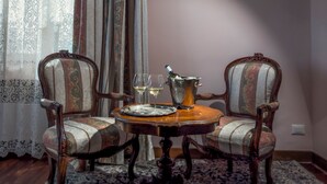 Um quarto com uma mesa de madeira, duas cadeiras estofadas, uma cortina de renda e um tapete estampado.