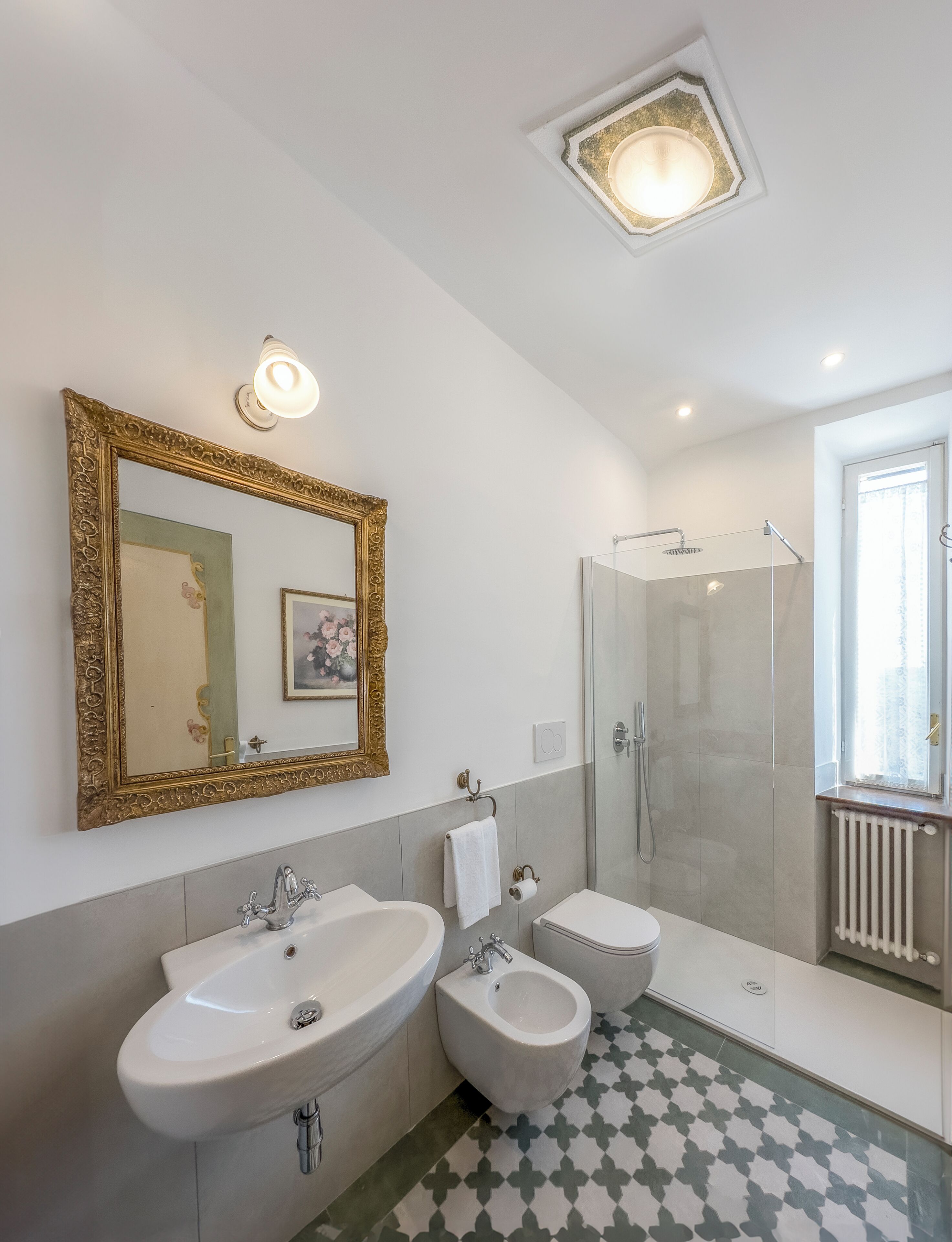 Een badkamer met twee wasbakken, een bidet, een douche en een spiegel met decoratieve lijst.