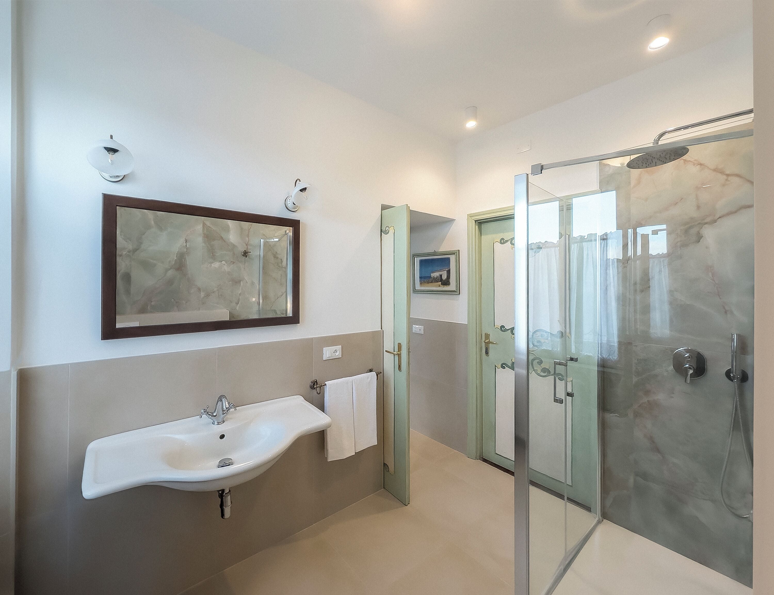 Une salle de bain moderne avec une douche à parois de verre, un mur recouvert de carreaux de marbre et un grand miroir au-dessus du lavabo.