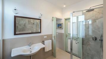 Une salle de bain moderne avec une douche à parois de verre, un mur recouvert de carreaux de marbre et un grand miroir au-dessus du lavabo.