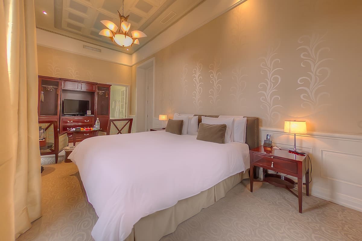 A hotel room with a large bed, a TV, a desk with a lamp, and a mirror.