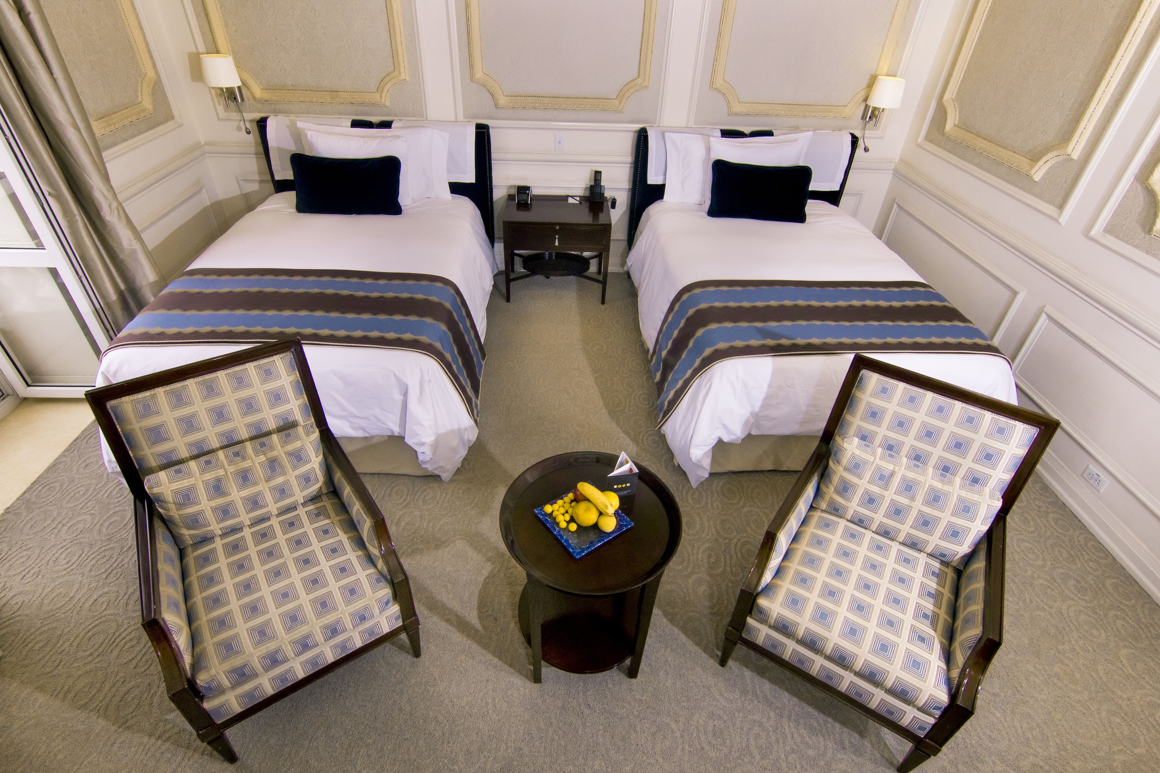 A hotel room with two beds, a small table with fruit, and two chairs.