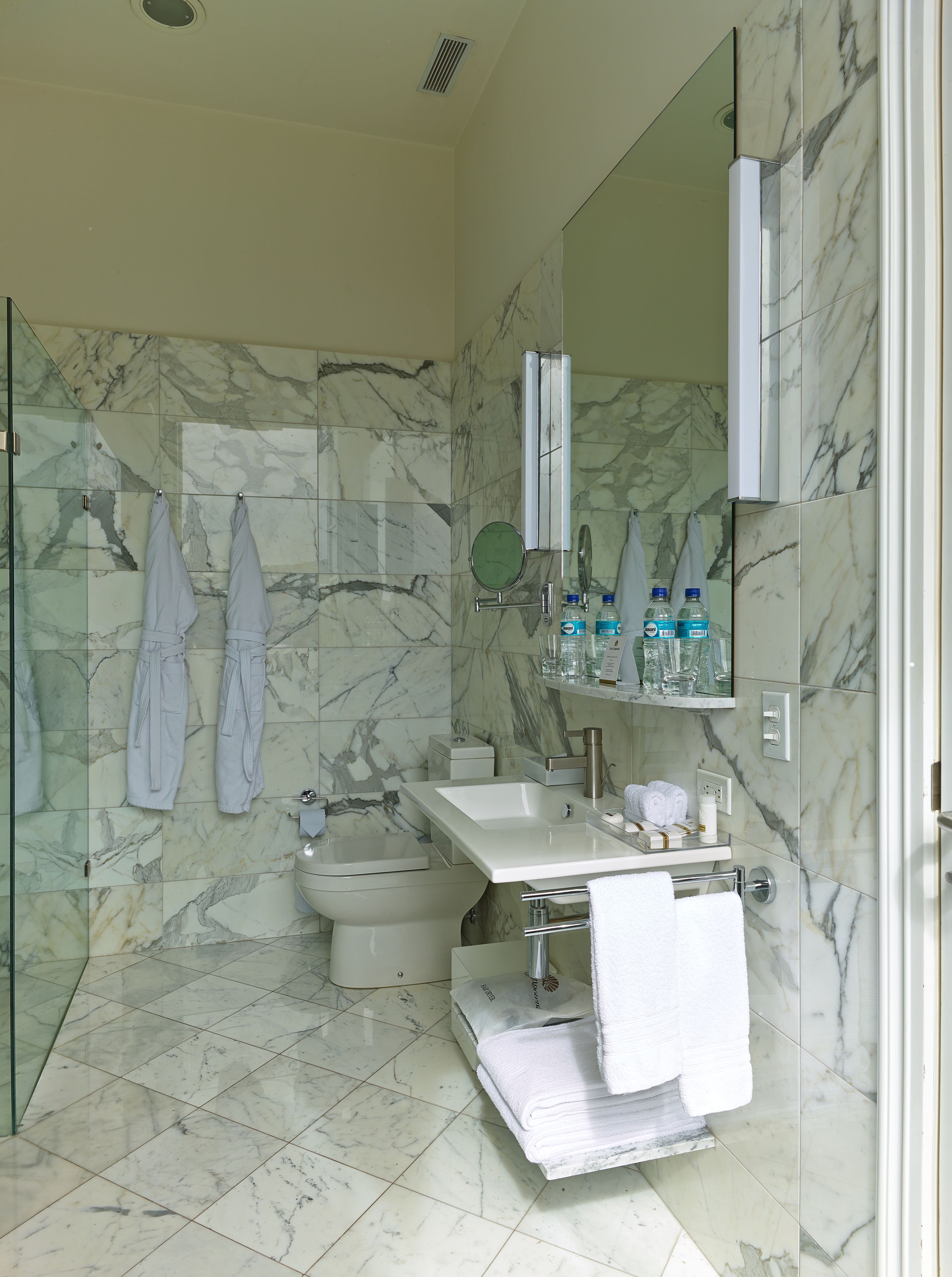 A modern bathroom with a marble floor, a glass shower enclosure, a white sink, and a large mirror.