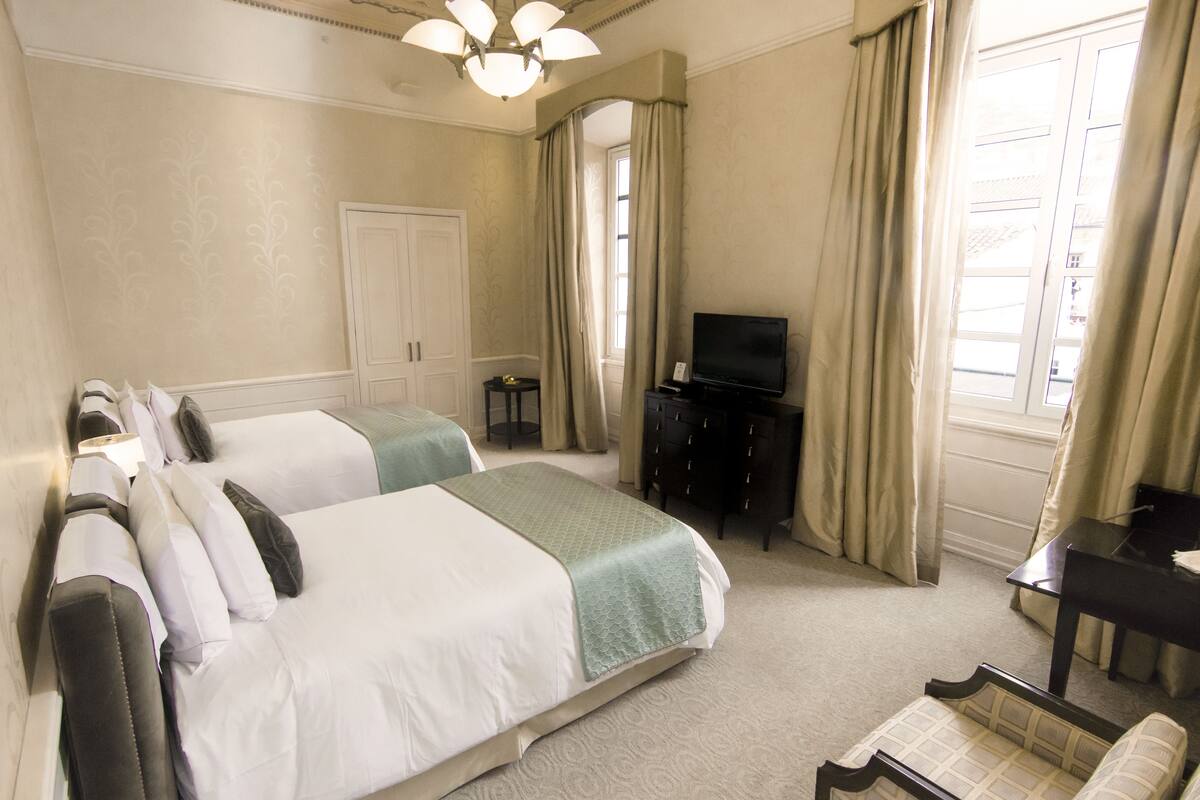 A hotel room with two beds, a television, a desk, and a window with curtains.