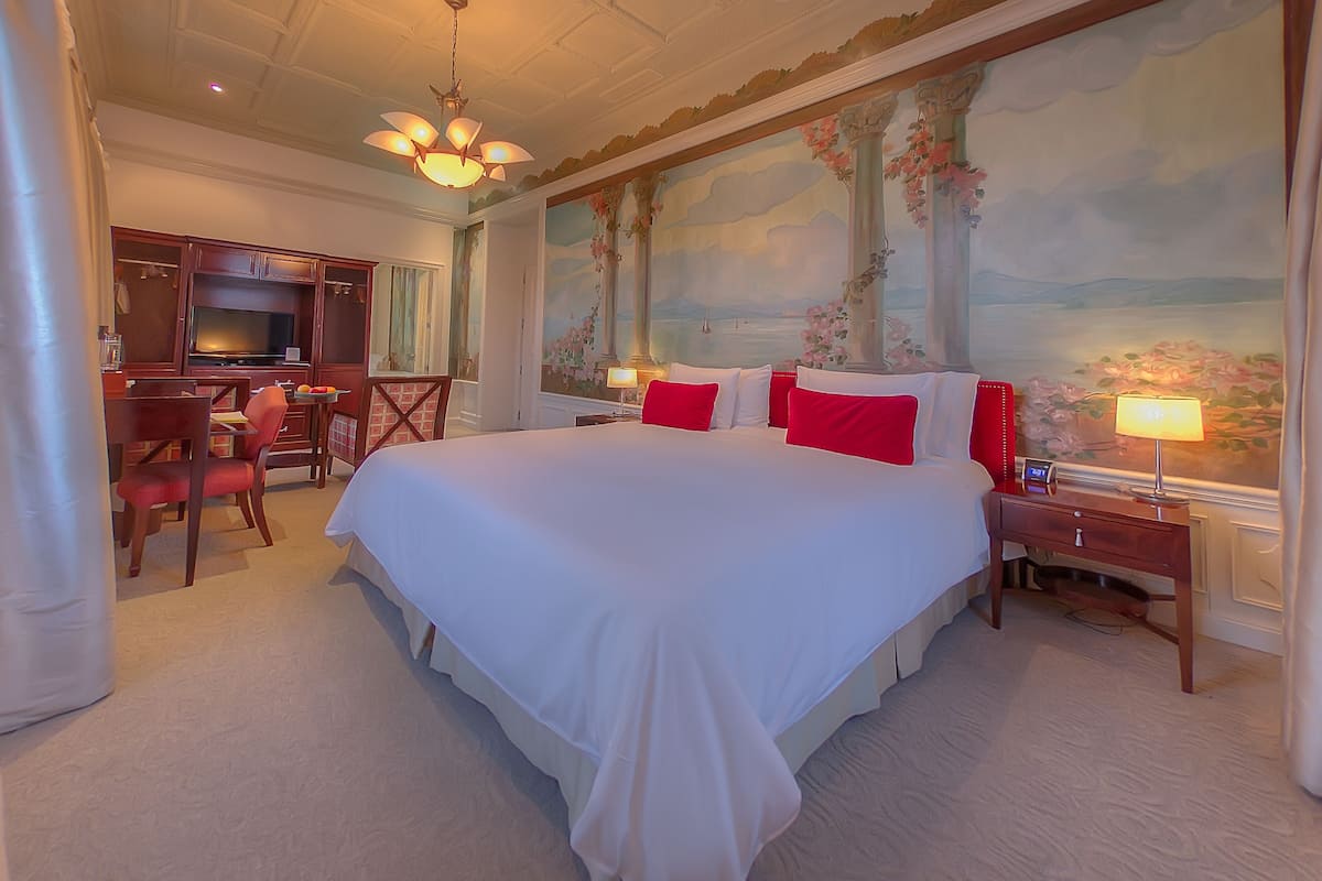 A hotel room with a large bed, a desk, a chair, a TV, and a painting on the wall.