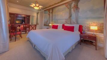 A hotel room with a large bed, a desk, a chair, a TV, and a painting on the wall.