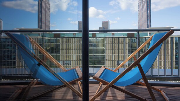 Een balkon met twee blauwe lounge fauteuils en een uitzicht op hoge gebouwen op de achtergrond.