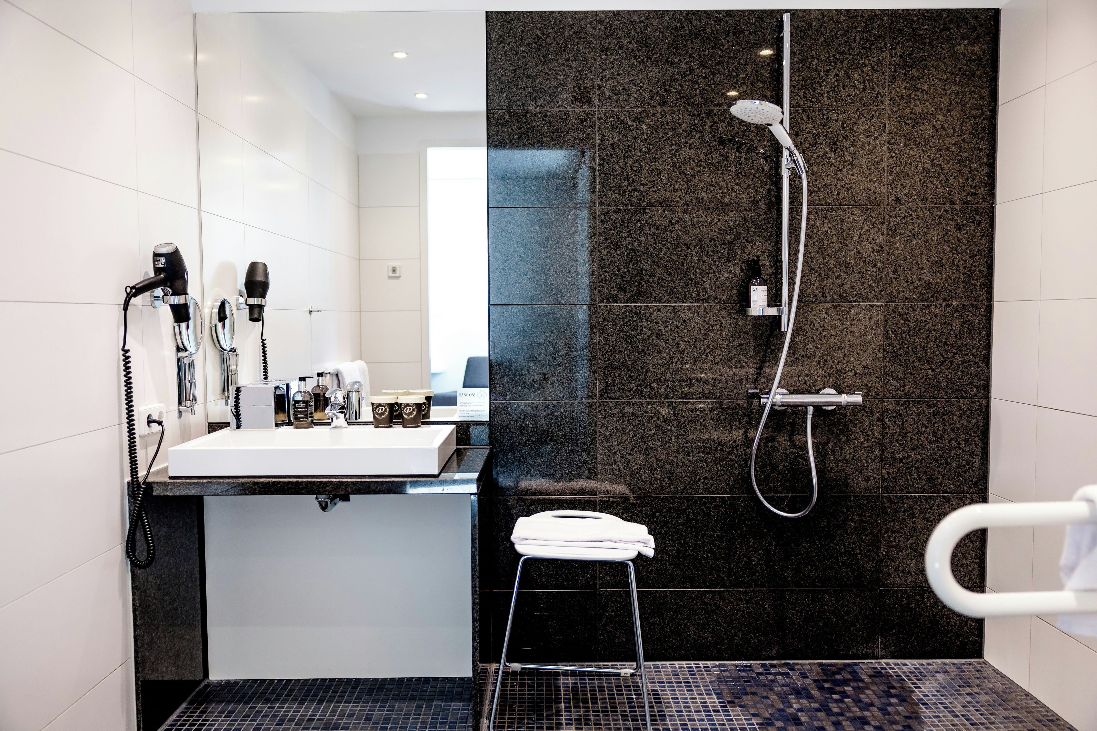 A modern bathroom with a sink, two hair dryers, a shower, and a towel rack.