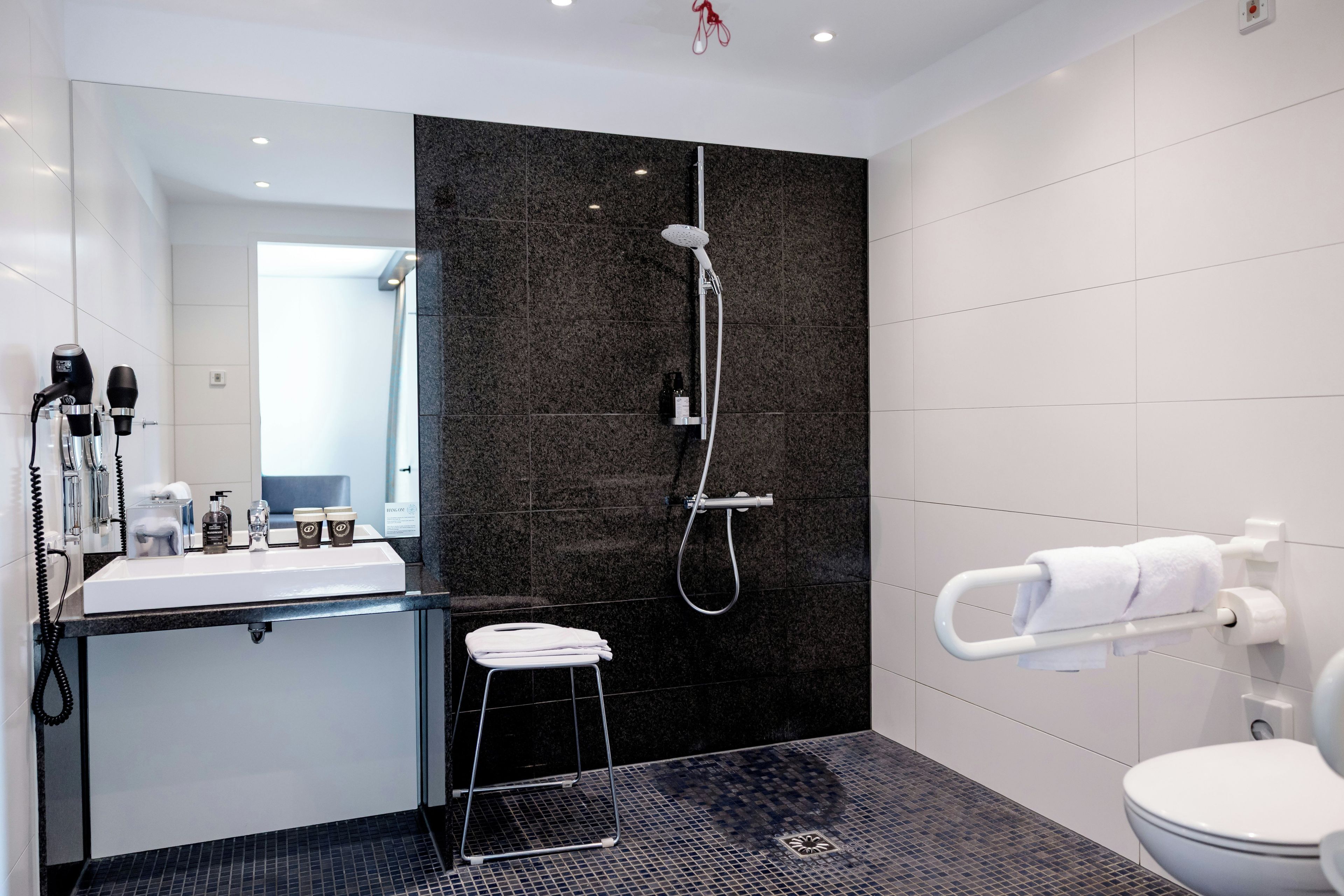 A modern bathroom with a black tiled shower wall, a white sink, and a toilet.