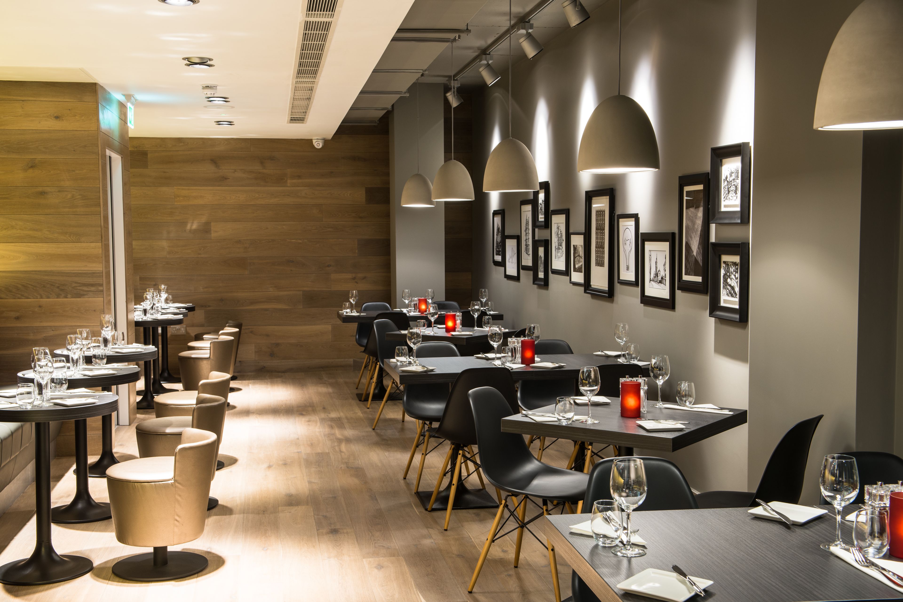 A restaurant with multiple tables and chairs, wooden flooring, and framed pictures on the walls.