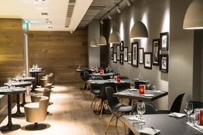 A restaurant with multiple tables and chairs, wooden flooring, and framed pictures on the walls.