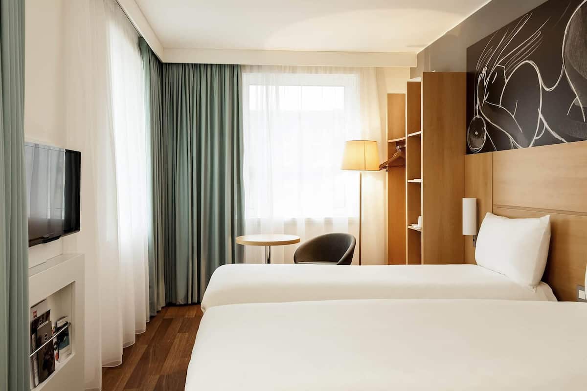Une chambre d’hôtel avec deux lits, une télévision, un bureau avec une lampe et une armoire.