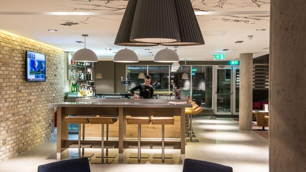 A modern bar area with a bartender, a brick wall, and a large pendant light.