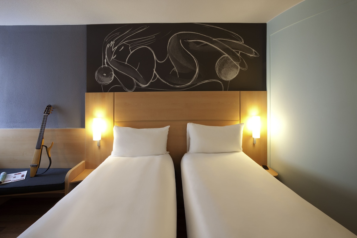 Habitación de hotel con dos camas, una guitarra y una obra de arte en la pared.