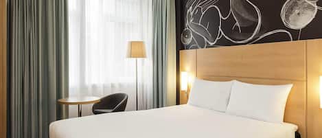 Una habitación de hotel con una cama grande, una mesita, una silla y una lámpara.