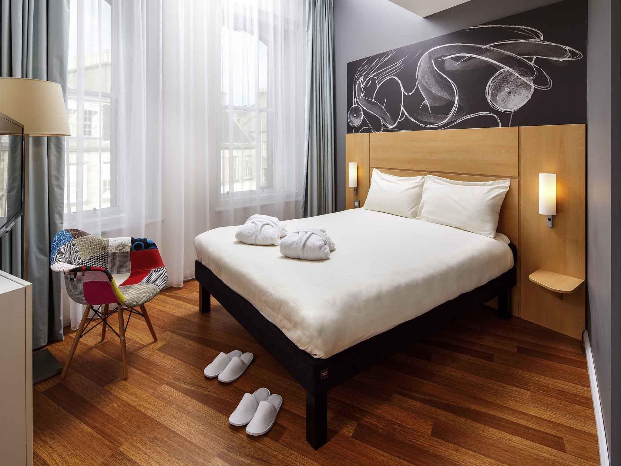 Hotelkamer met een bed, een stoel, een kunstwerk aan de muur en een raam met gordijnen.