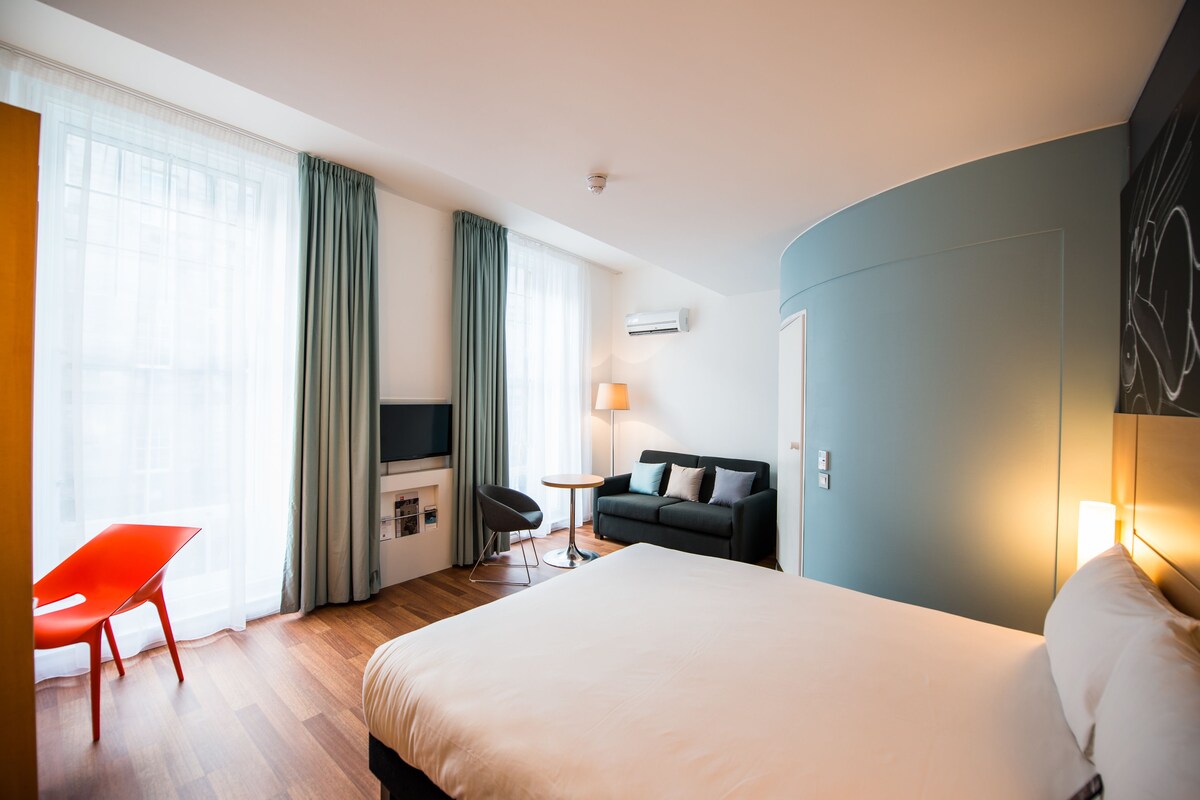 Una habitación de hotel con una cama grande, un escritorio con silla, un sofá y un televisor.