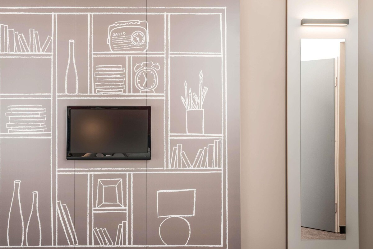 Une chambre moderne dotée d’un téléviseur à écran plat fixé au mur, lequel est décoré comme un tableau noir.