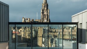 A modern building with large glass windows overlooking a historic church with a clock tower.