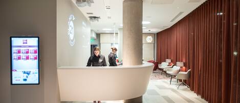 A modern reception area with a curved reception desk, a digital display, and a seating area with red curtains.